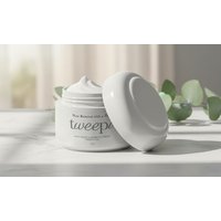 White Tweepro cream jar with open lid, displaying smooth whipped texture, on a light surface with green leaves in background.