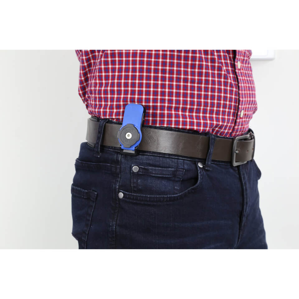 Black Quad Lock Belt Utility Clip attached to a brown leather belt, featuring a circular mounting plate and a sturdy design, worn with dark blue jeans and a checkered shirt.