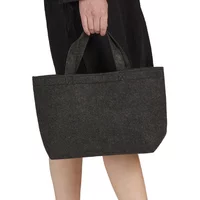 Small black felt tote bag with short handles, carried by a person wearing a black outfit.