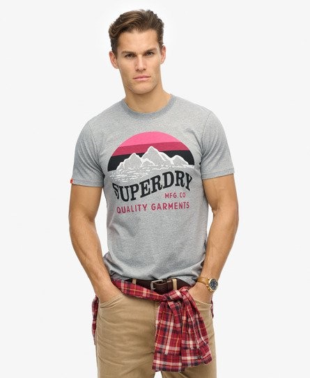 Gray cotton T-shirt featuring a bold graphic print with mountains and "SUPERDRY" text in red and black, worn with a plaid shirt tied around the waist.