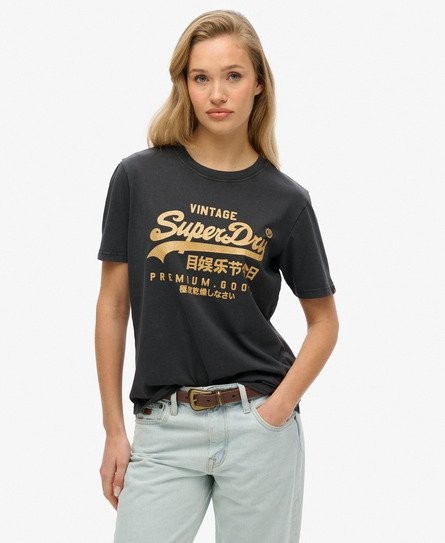 Casual black T-shirt for women by Superdry featuring a vintage logo in gold, made from soft material, paired with light blue jeans and a brown belt.