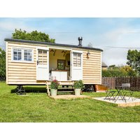 Wooden shepherd's hut with white doors, large windows, and small porch, set in a grassy area with outdoor seating.