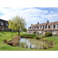 Cottages with brown roofs by a pond and willow tree under a blue sky, part of "High Tide" by cottages.com.