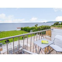 Balcony view from "On The Beach" cottage, featuring a metal table and chairs overlooking a grassy area and the sea.
