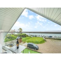 Triangular glass balcony with ocean view, wine bottle on table, overlooking grassy area and parked car.