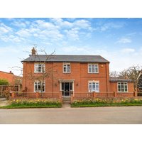 Red brick two-story cottage with white framed windows, black roof, and front garden, under a blue sky.