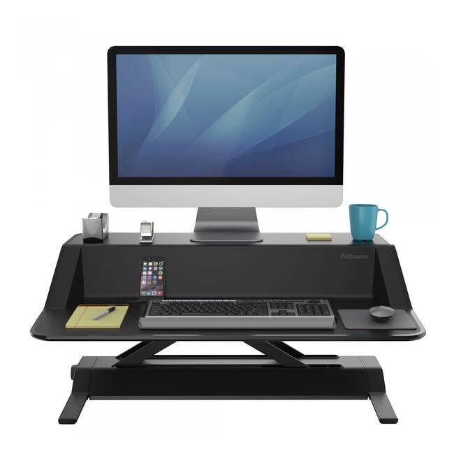 Black height-adjustable desk riser with a sleek design, featuring a spacious top for a monitor, a keyboard tray, and compartments for stationery and a coffee mug.