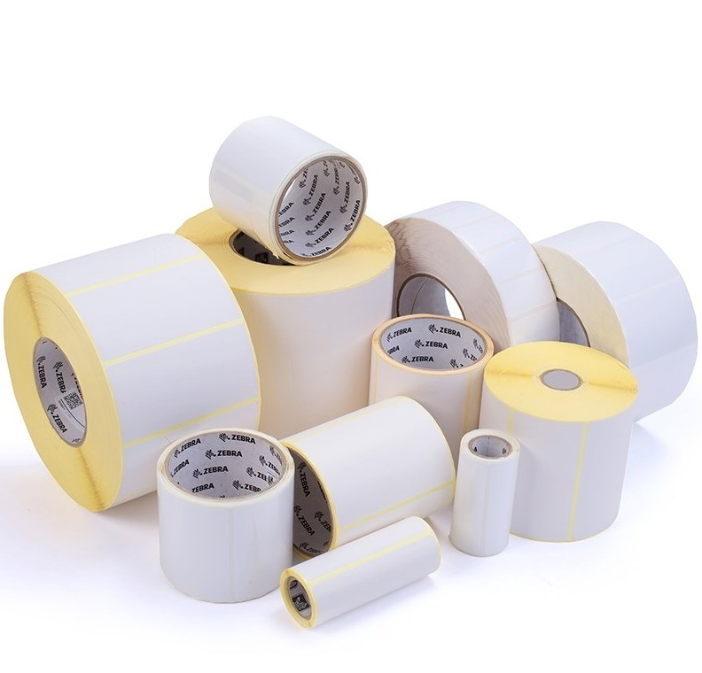 White self-adhesive printer labels in various sizes and rolls, featuring a smooth surface and a yellow backing, branded with the Zebra logo.