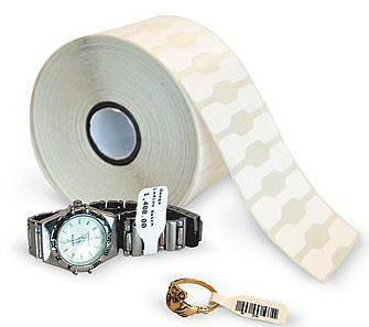 White self-adhesive printer label roll by Zebra, featuring a smooth finish and multiple blank labels, alongside a silver watch and a gold ring for scale.