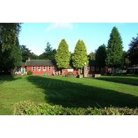 Red brick building surrounded by lush green lawn and tall trees, part of a fitness retreat in West Linton, Edinburgh.