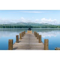 Wooden pier extending into Lake Windermere with scenic mountain backdrop and clear blue sky.