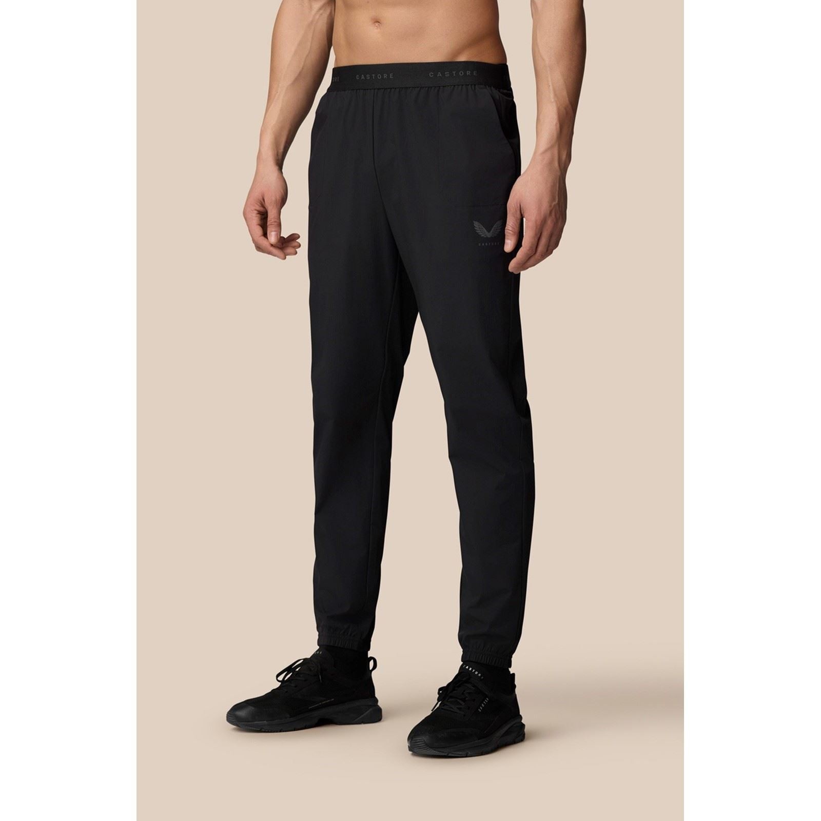 Black polyester joggers with a woven texture, featuring an elastic waistband, side pocket, and tapered fit, designed for men's activewear by Castore.