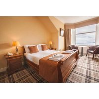 Hotel room with a double bed, plaid carpet, bedside lamps, and a window view of the sea.
