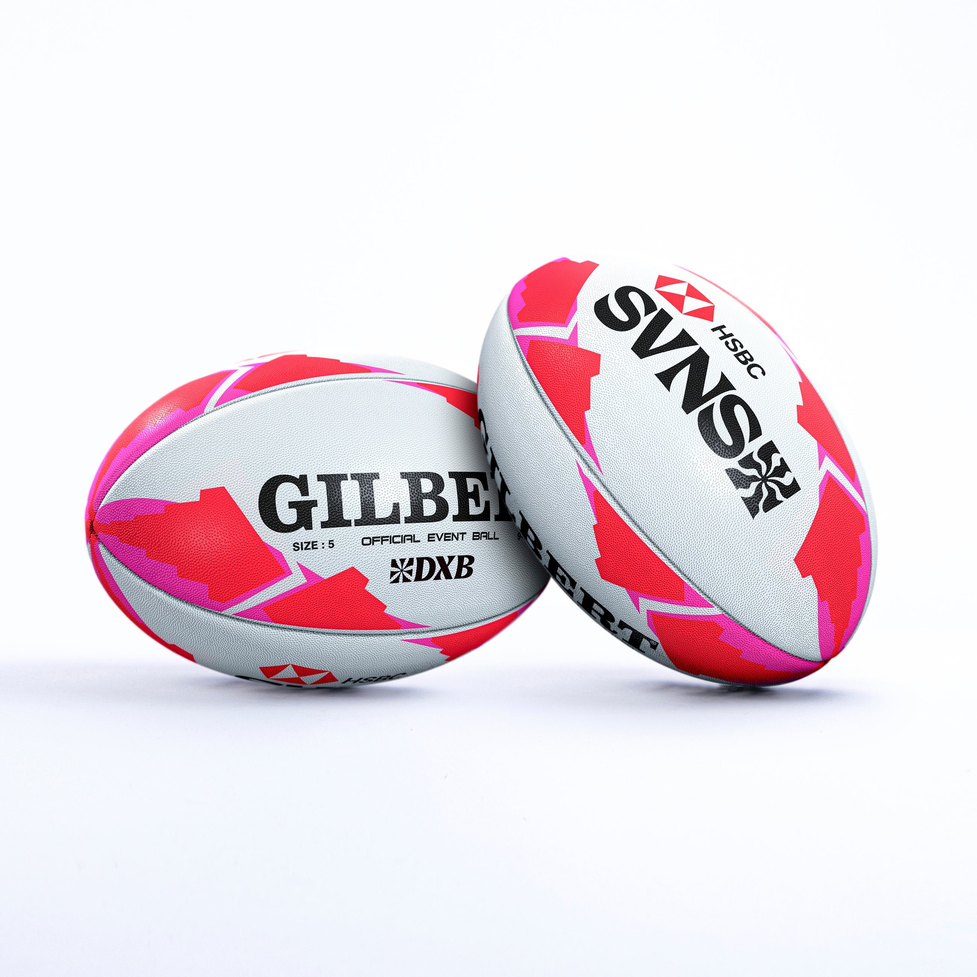 Two rugby balls featuring a white base with vibrant pink and red geometric patterns, labeled "GILBERT" and "SVNS" with the HSBC logo, designed for the Dubai 23/24 season.