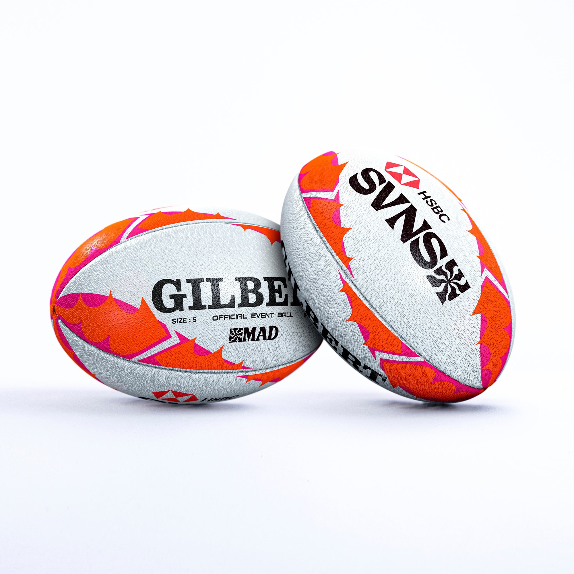 Two rugby balls featuring a white base with vibrant orange and pink accents, branded with "GILBERT" and "SVNS" logos, designed for the HSBC Madrid event.