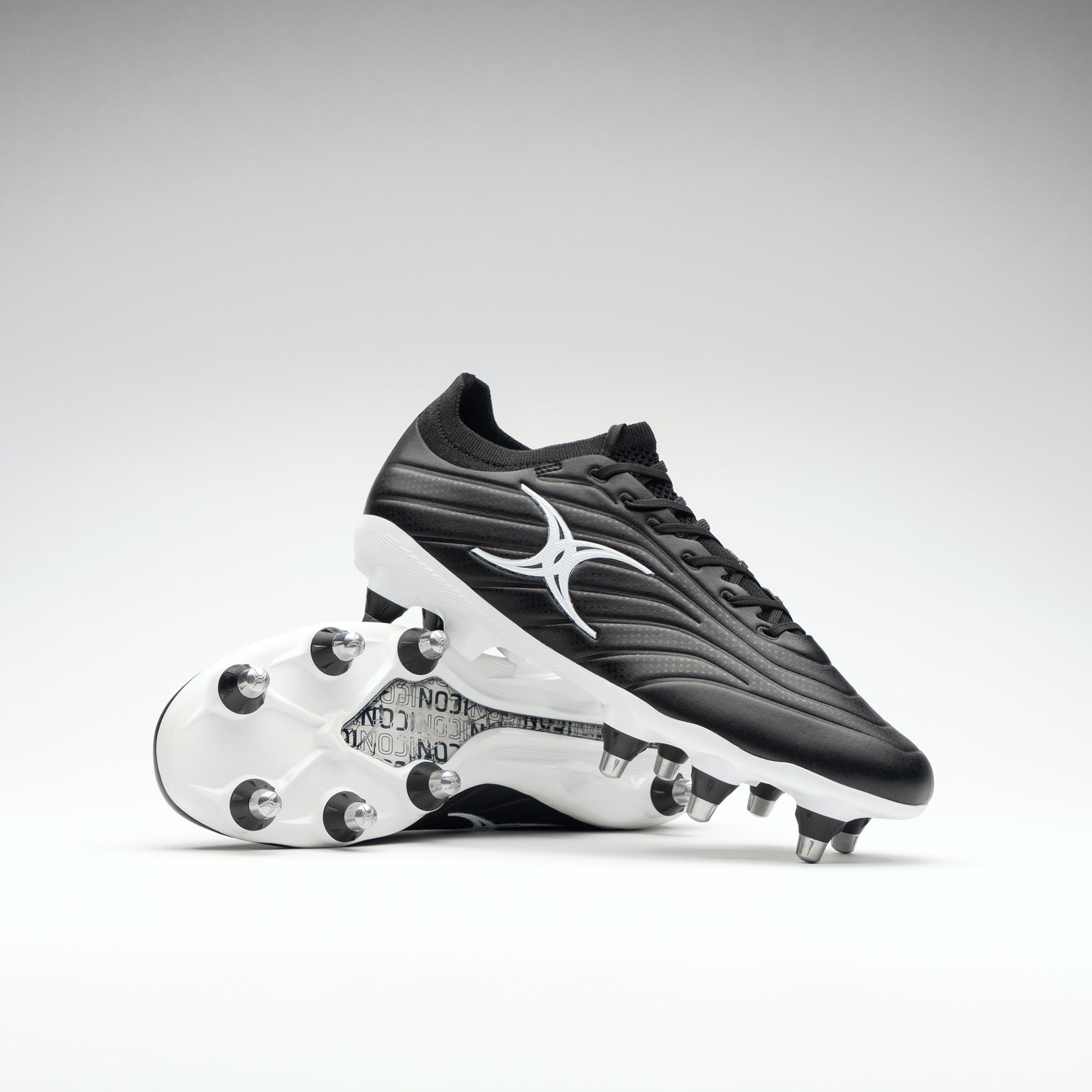 Black junior rugby boots with a sleek design, featuring a white logo, synthetic upper, and eight metal studs on the sole for traction on the field.