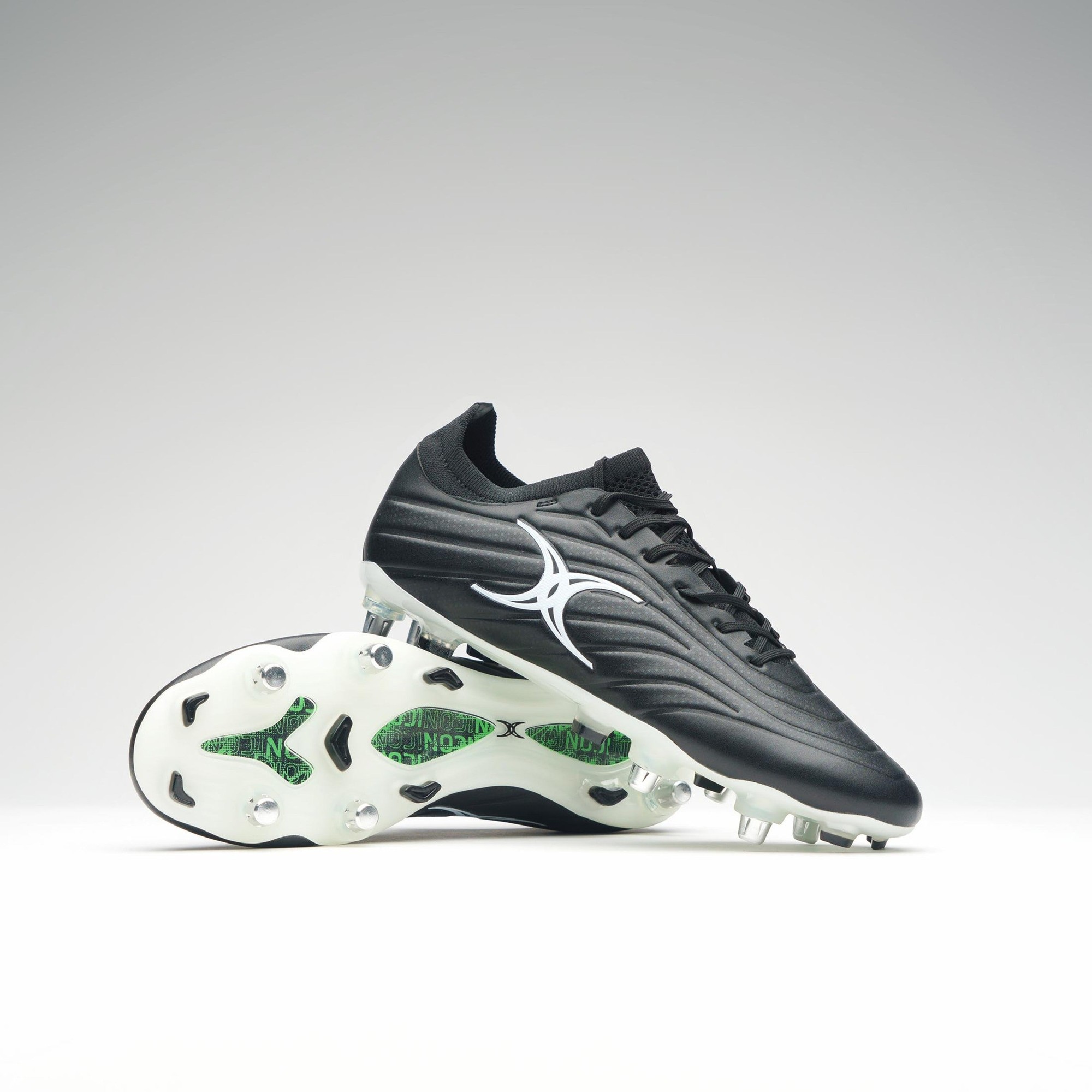Black junior rugby boots featuring a sleek design, synthetic upper, and six studded outsole for traction, with a white Gilbert logo on the side.