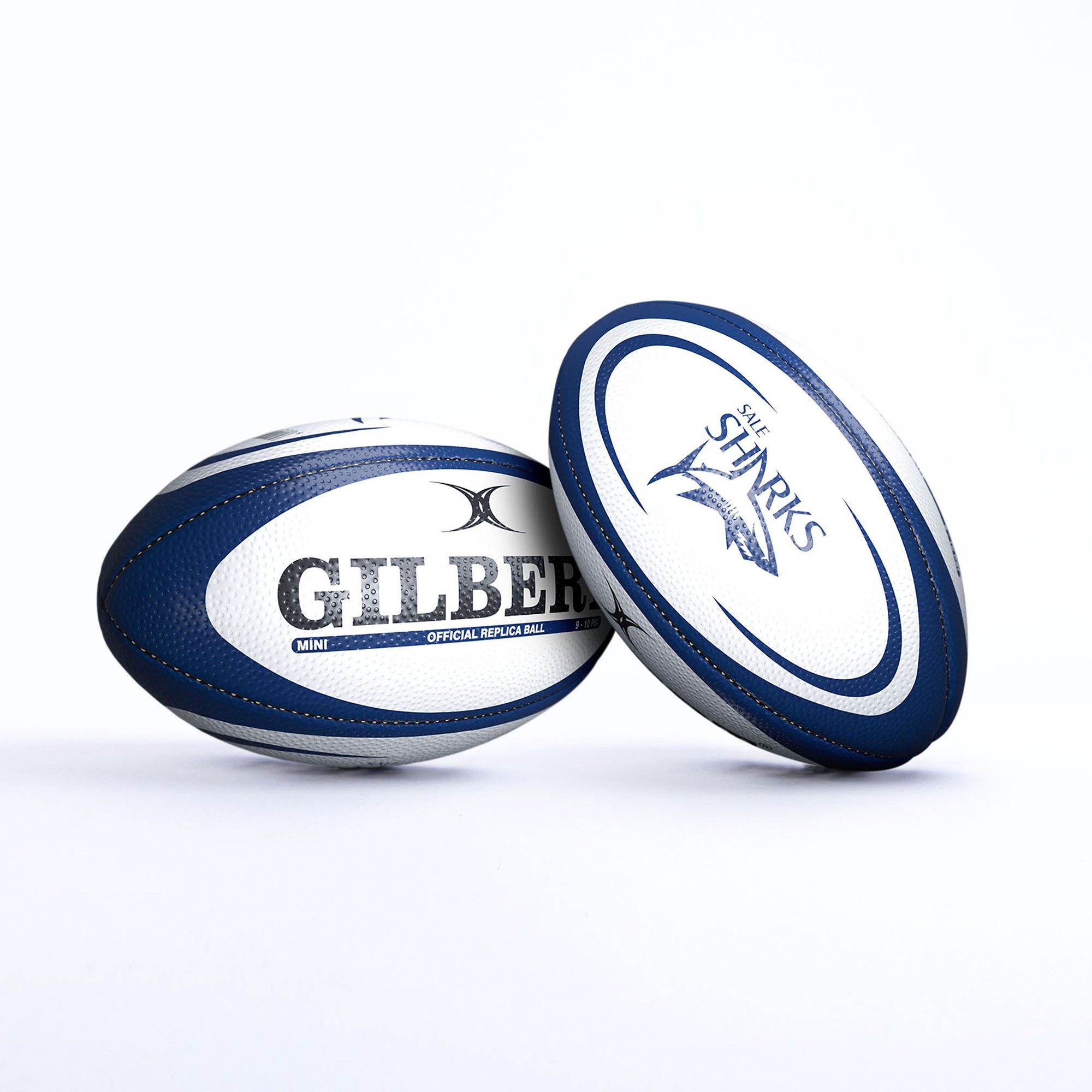 Blue and white Gilbert Rugby Sale Sharks replica ball featuring the brand name "GILBERT" and "SHARKS" logo, made of textured synthetic material for grip.