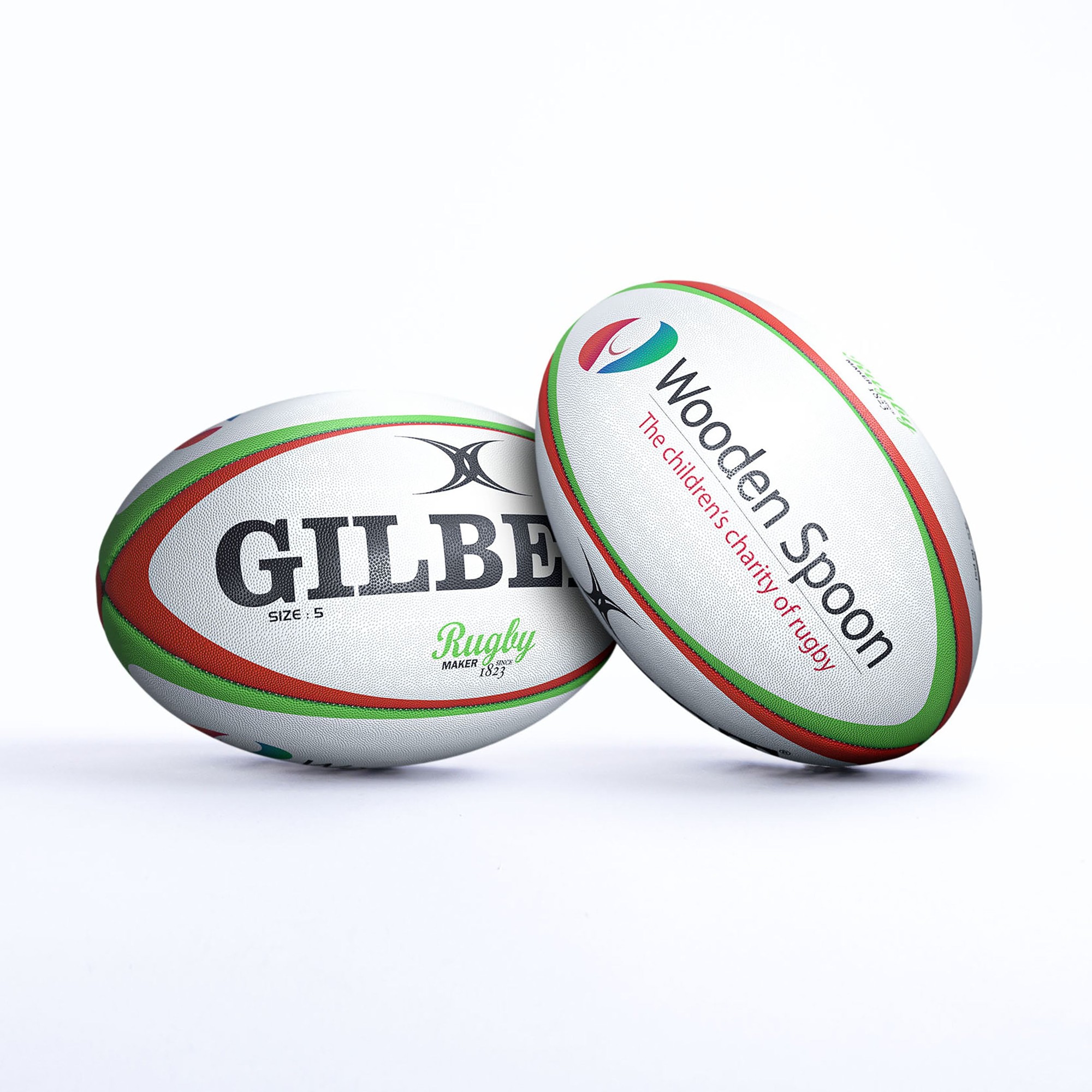 White rugby balls with red and green accents, featuring "GILBERT" and "Wooden Spoon" logos, showcasing a smooth surface and classic oval shape.