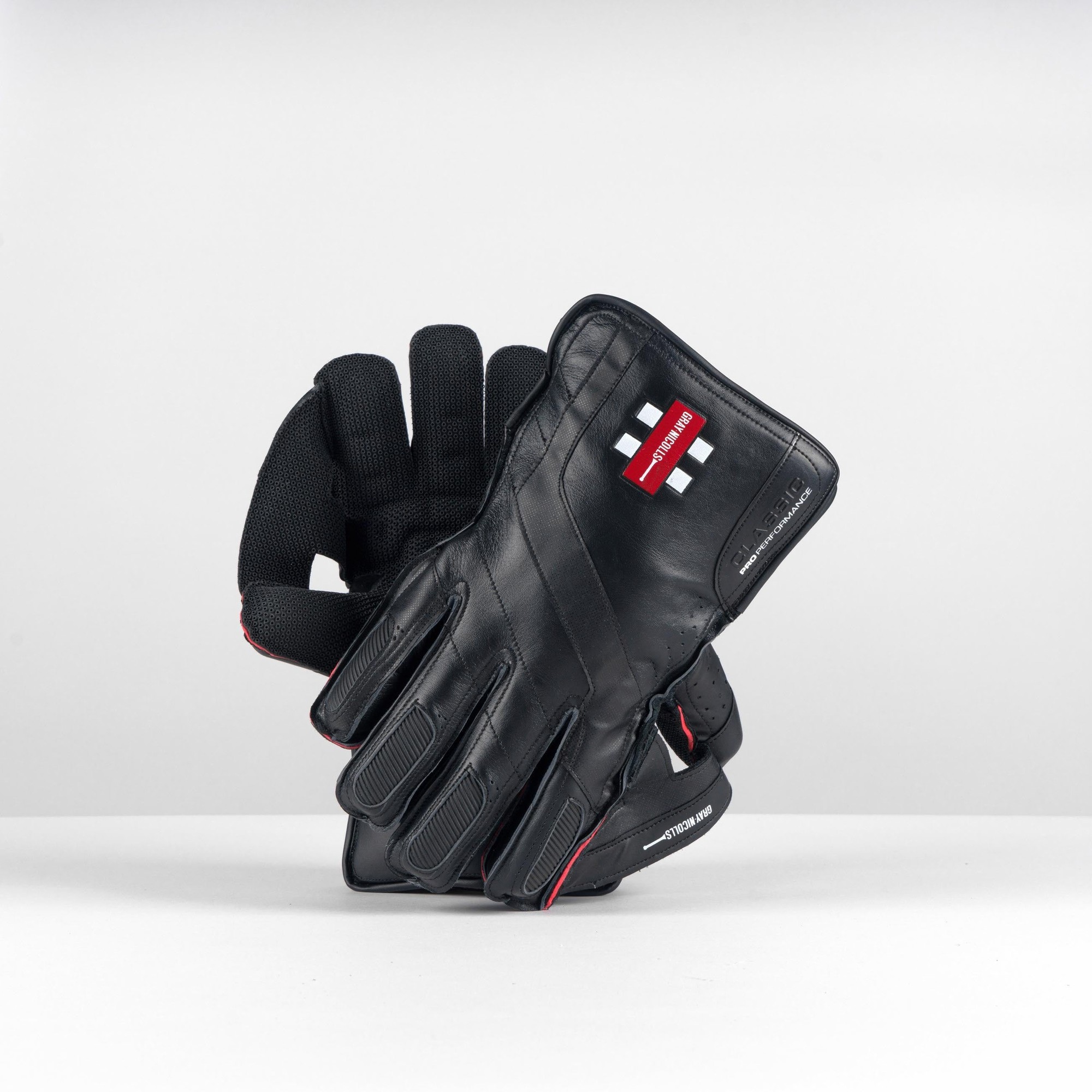 Black leather Gray-Nicolls Classic Pro Performance wicketkeeping gloves featuring padded fingers, a textured grip, and red accents for enhanced performance.