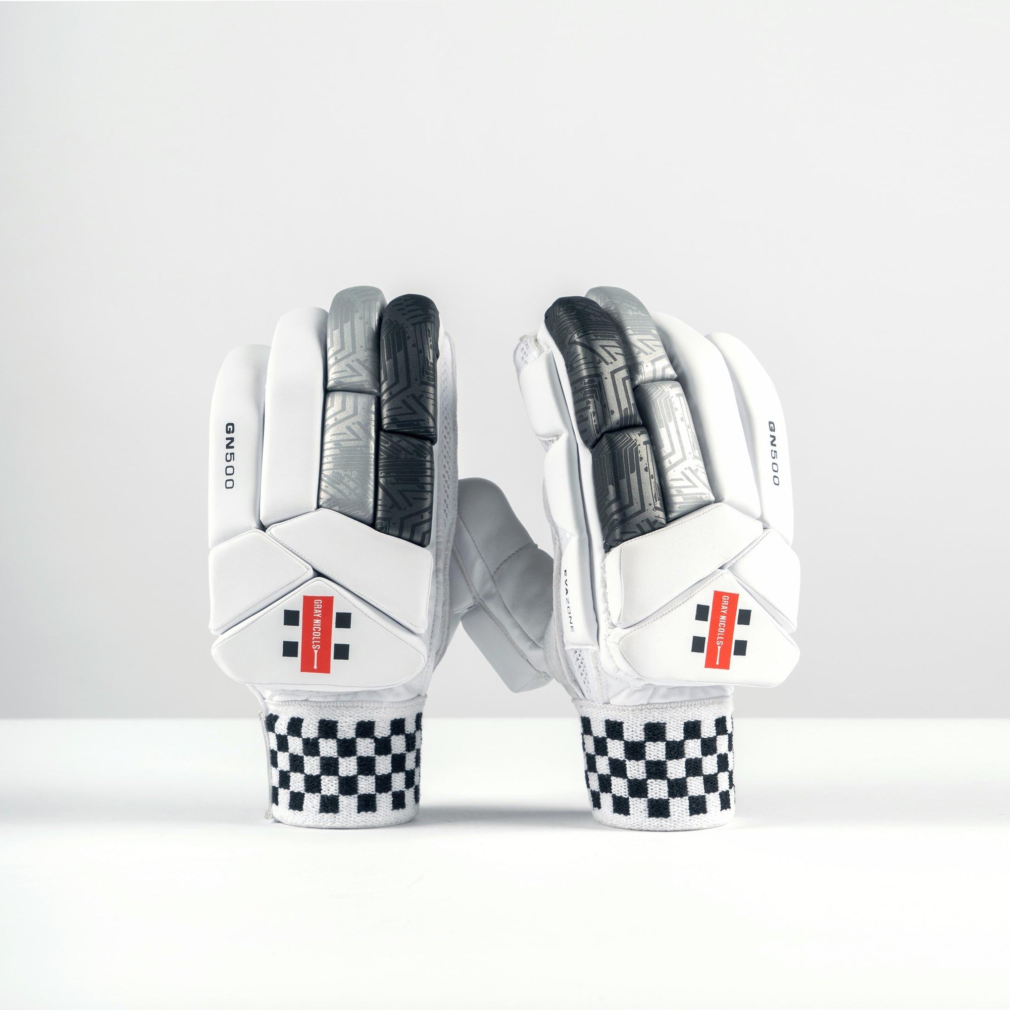 Gray-Nicolls GN500X junior batting gloves in white with black accents, featuring padded protection, textured grip, and a checkered wristband for secure fit.