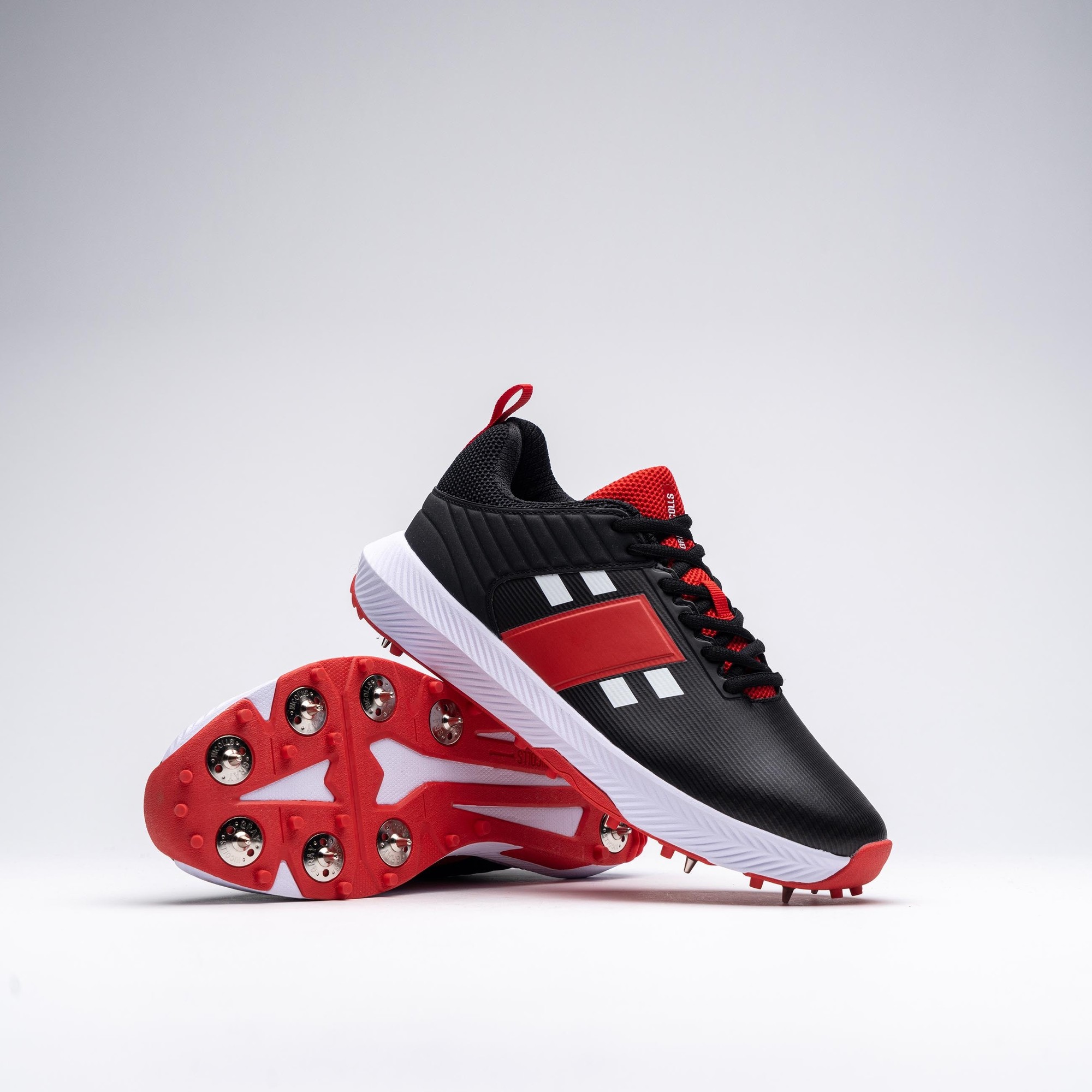 Gray-Nicolls Players 3.0 black adult spike shoes featuring a sleek black upper with red accents, white stripes, and a red and white studded sole for traction.