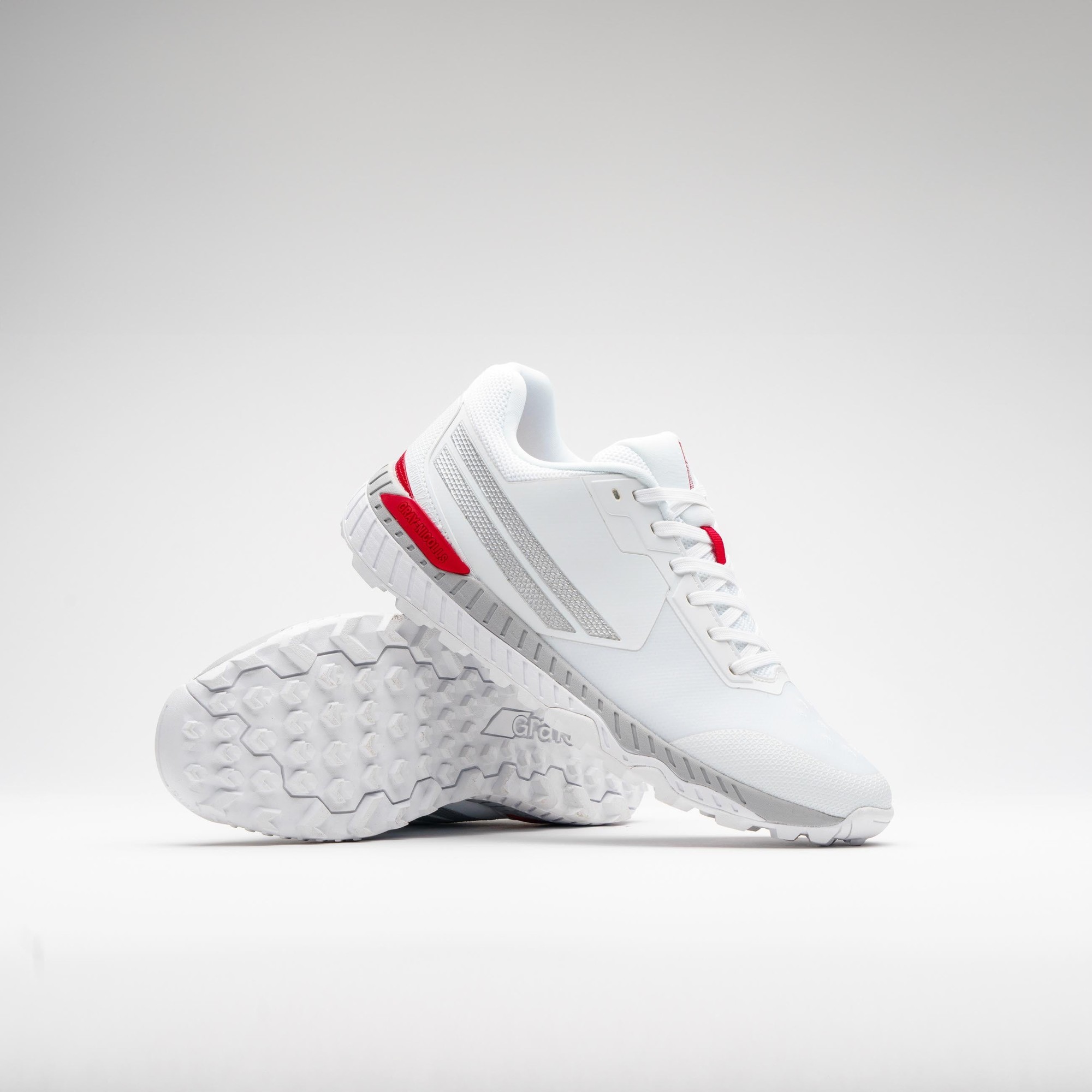 Gray-Nicolls Revo Pro 2.0 batting shoes in white with red accents, featuring a sleek design, breathable material, and a textured outsole for grip.