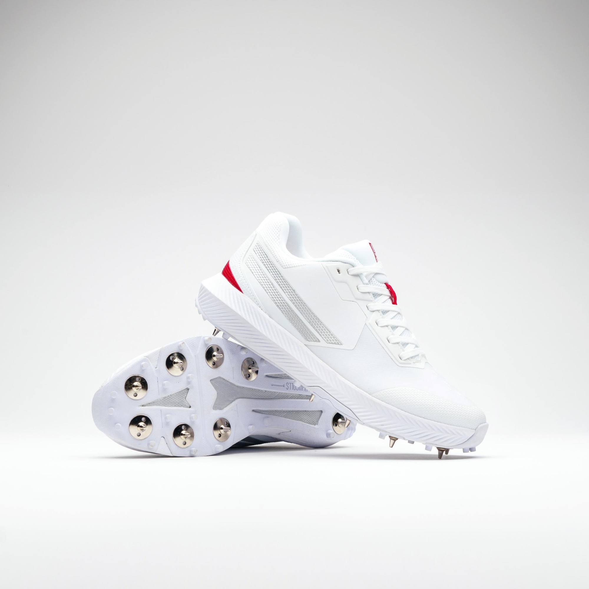 White Gray-Nicolls Revo Pro 2.0 spike shoes feature a sleek design with red accents, a textured upper, and a studded outsole for enhanced traction on the field.