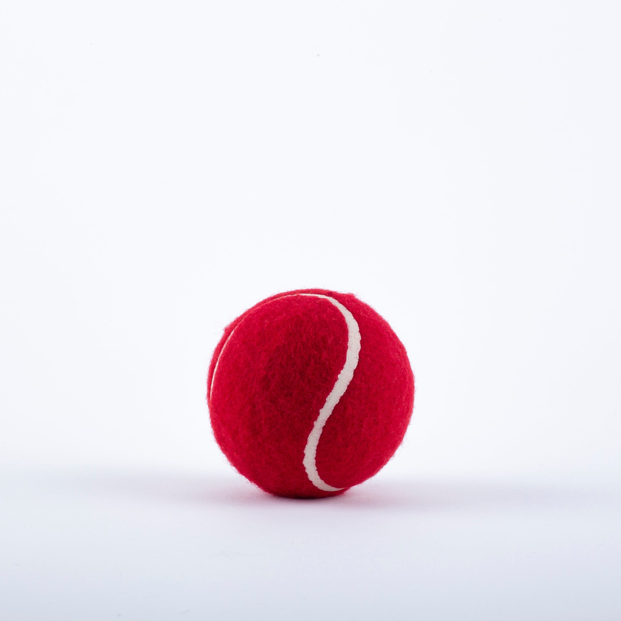 Red felt tennis ball with a white spiral seam, featuring a smooth surface and round shape, designed for use in tennis by Gray-Nicolls.