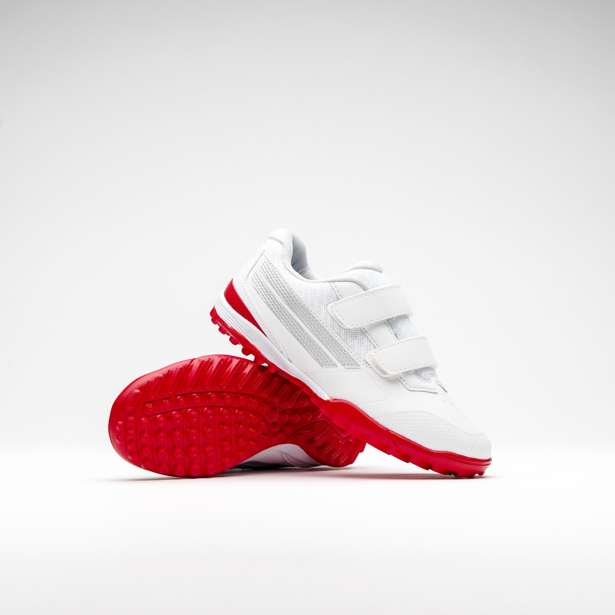 Gray-Nicolls Velocity 5.0 rubber shoes in white with red soles, featuring a sleek design, two adjustable Velcro straps, and a textured upper for enhanced grip.