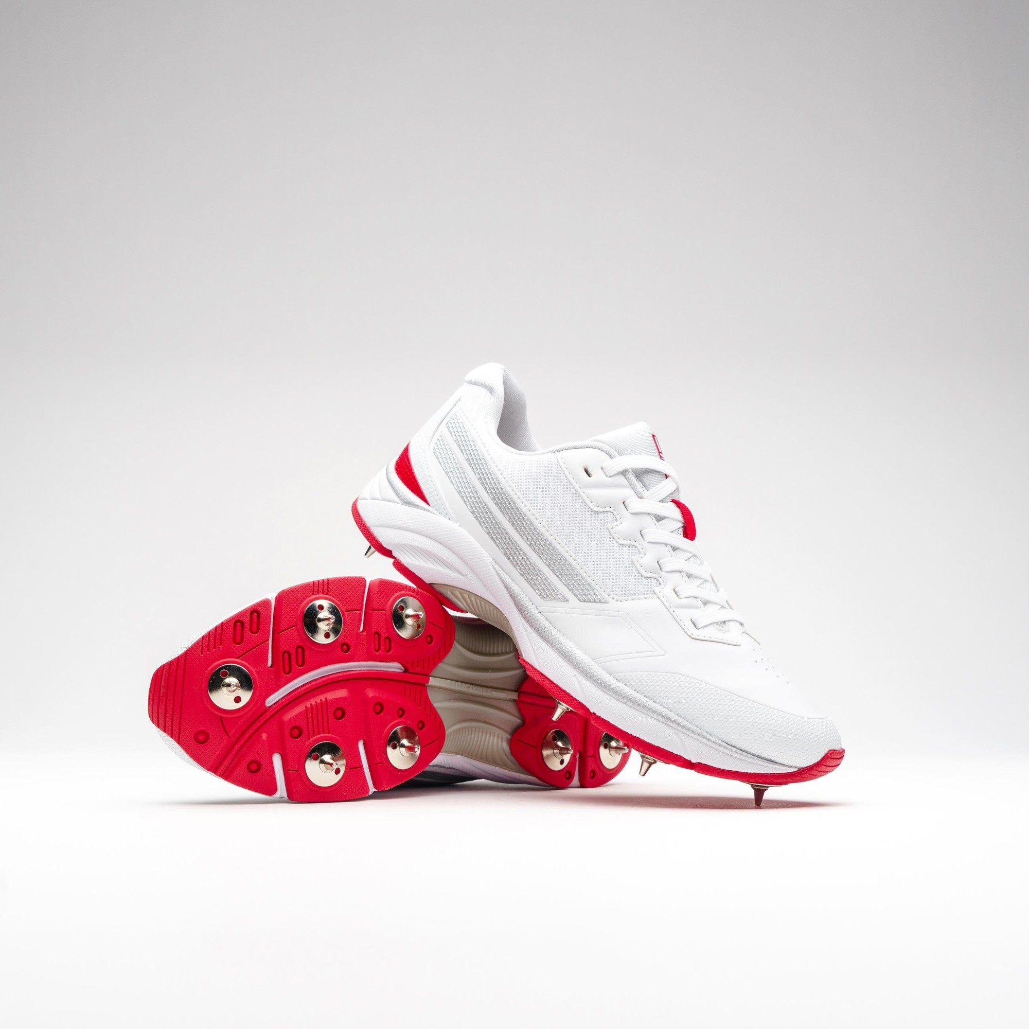 White Gray-Nicolls Velocity 5.0 spike shoes featuring a sleek design, breathable mesh panels, and red accents, with a spiked outsole for enhanced traction.
