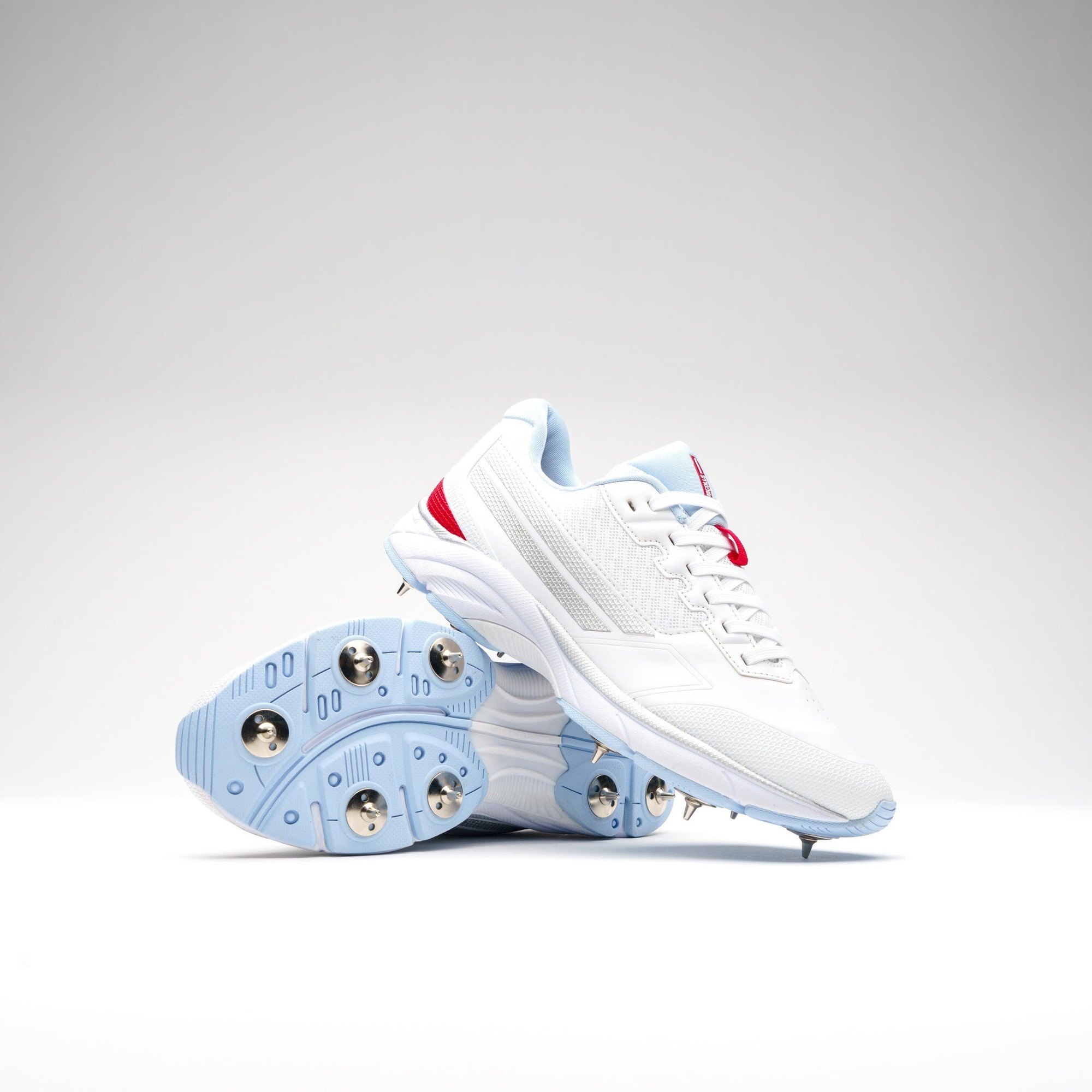 White Gray-Nicolls Velocity 5.5 spike shoes featuring a sleek design, blue accents, and metal spikes on the sole for enhanced traction on the field.