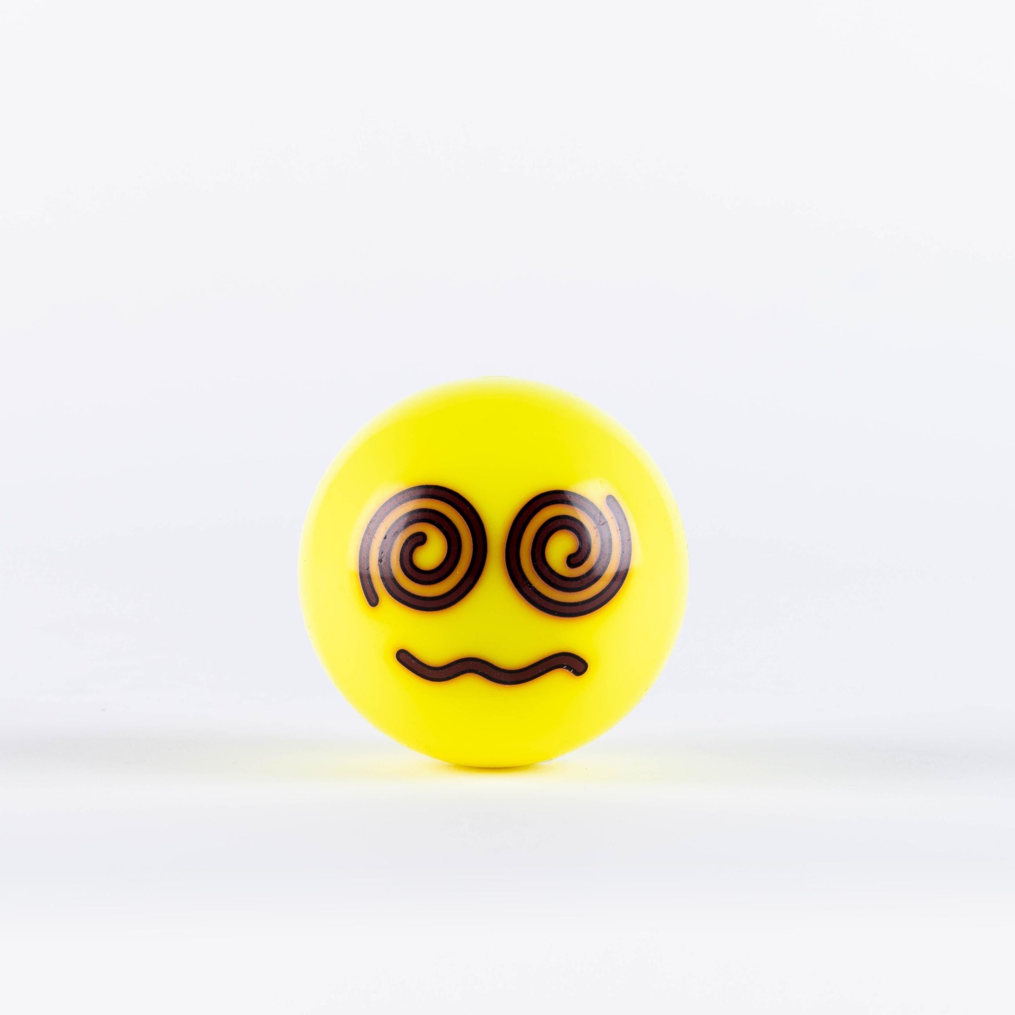 Fluo yellow hockey ball with a smiling emoji face featuring spiral eyes and a wavy mouth, made of durable plastic for enhanced visibility during play.