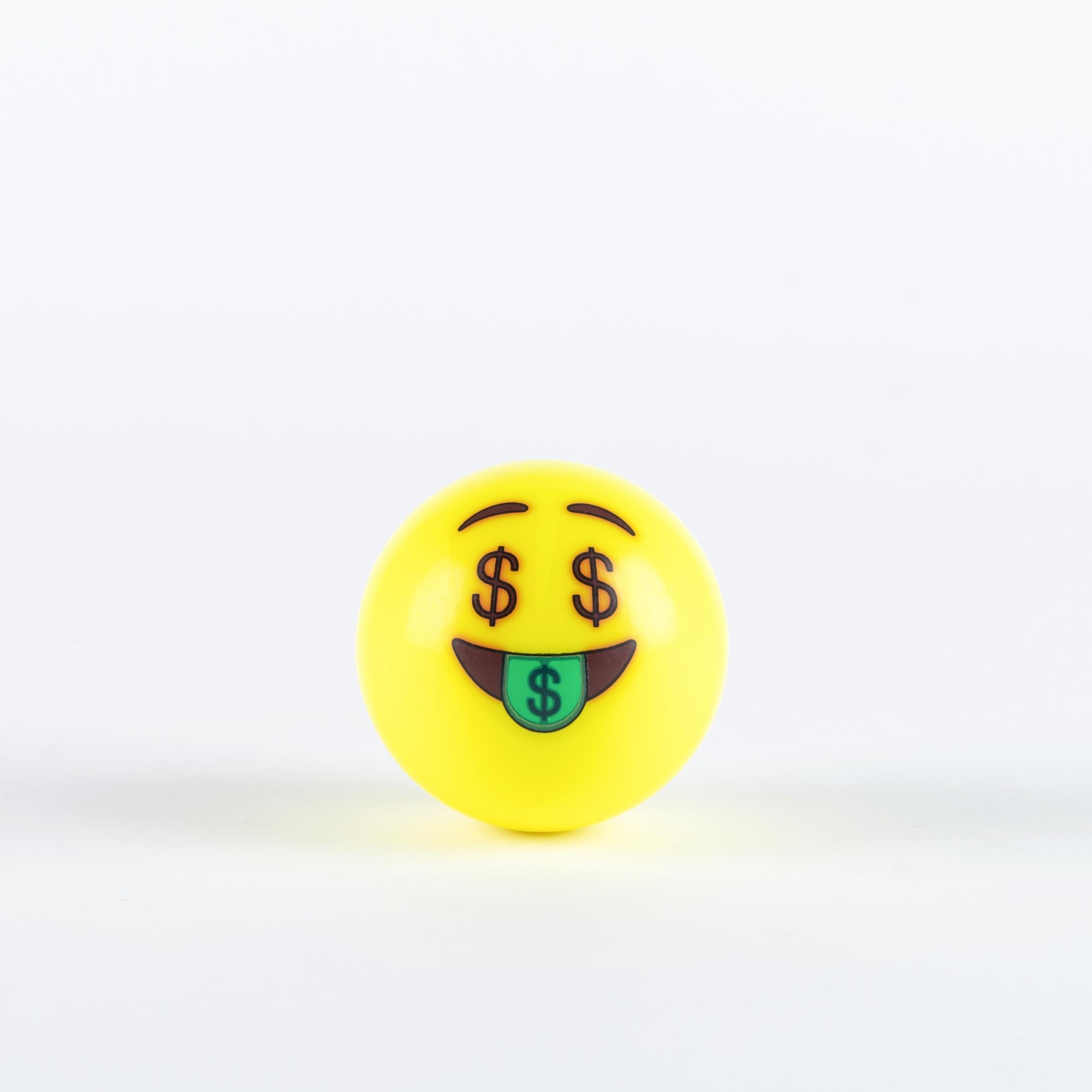 Fluo yellow hockey ball featuring a smiling emoji face with dollar signs for eyes and a tongue sticking out, made of durable plastic material.