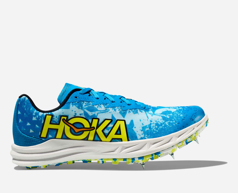 Unisex Hoka Crescendo XC shoe in Dive Blue and Evening Primrose, featuring a vibrant blue upper, prominent yellow logo, and spiked outsole for traction.