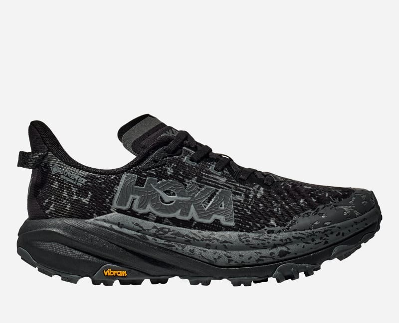 Black Hoka Speedgoat 6 GTX women's trail running shoes with a textured upper, wide fit, and Vibram outsole, featuring a prominent HOKA logo and a sleek design.