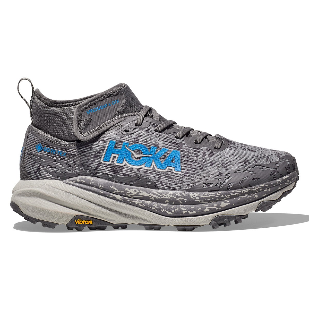 Hoka Speedgoat 6 Mid Gore-tex in Satellite Grey and Stardust features a grey upper with blue logo, a high ankle design, and a rugged Vibram sole for enhanced traction.