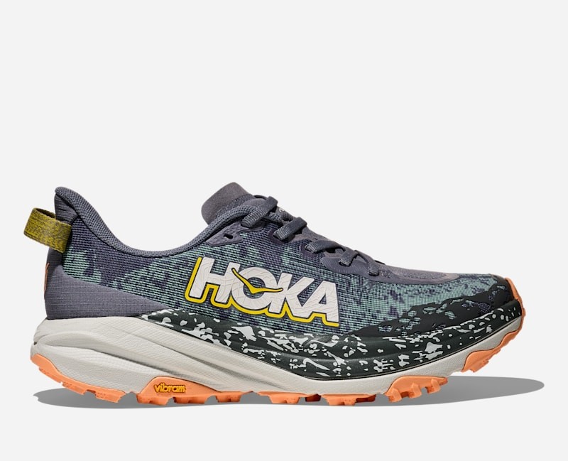 HOKA Women's Speedgoat 6 Trail Shoes in Grey Skies/Cosmic Grey feature a lightweight design, vibrant orange outsole, and a textured upper with a prominent HOKA logo.