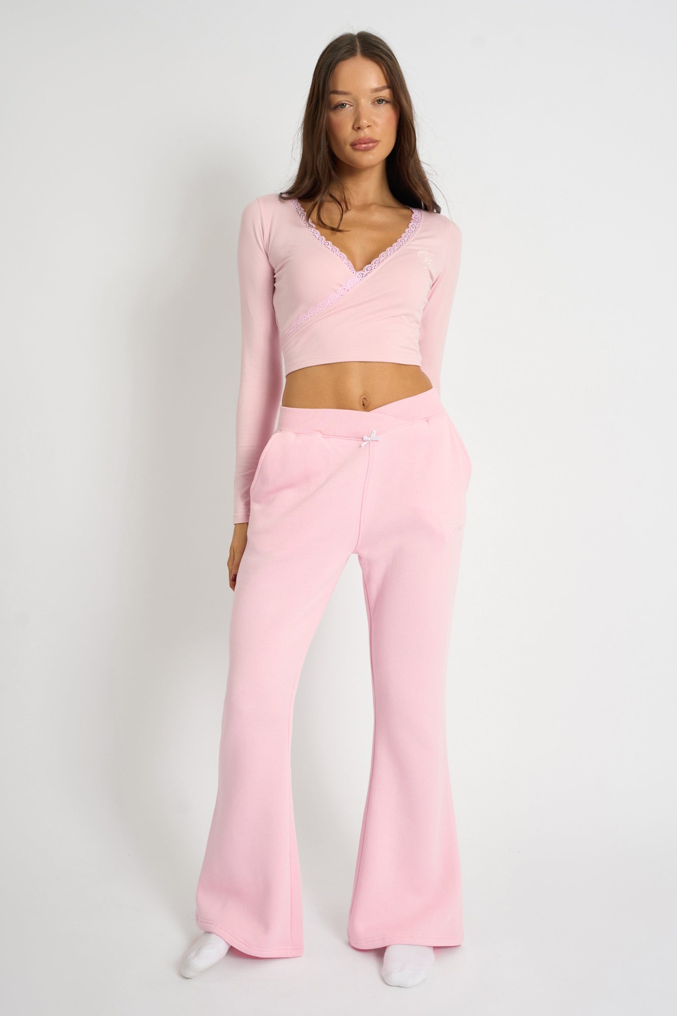 Pink wide-leg joggers with bow detail at the waist, made from soft fabric, paired with a matching long-sleeve top featuring a v-neckline and delicate trim.