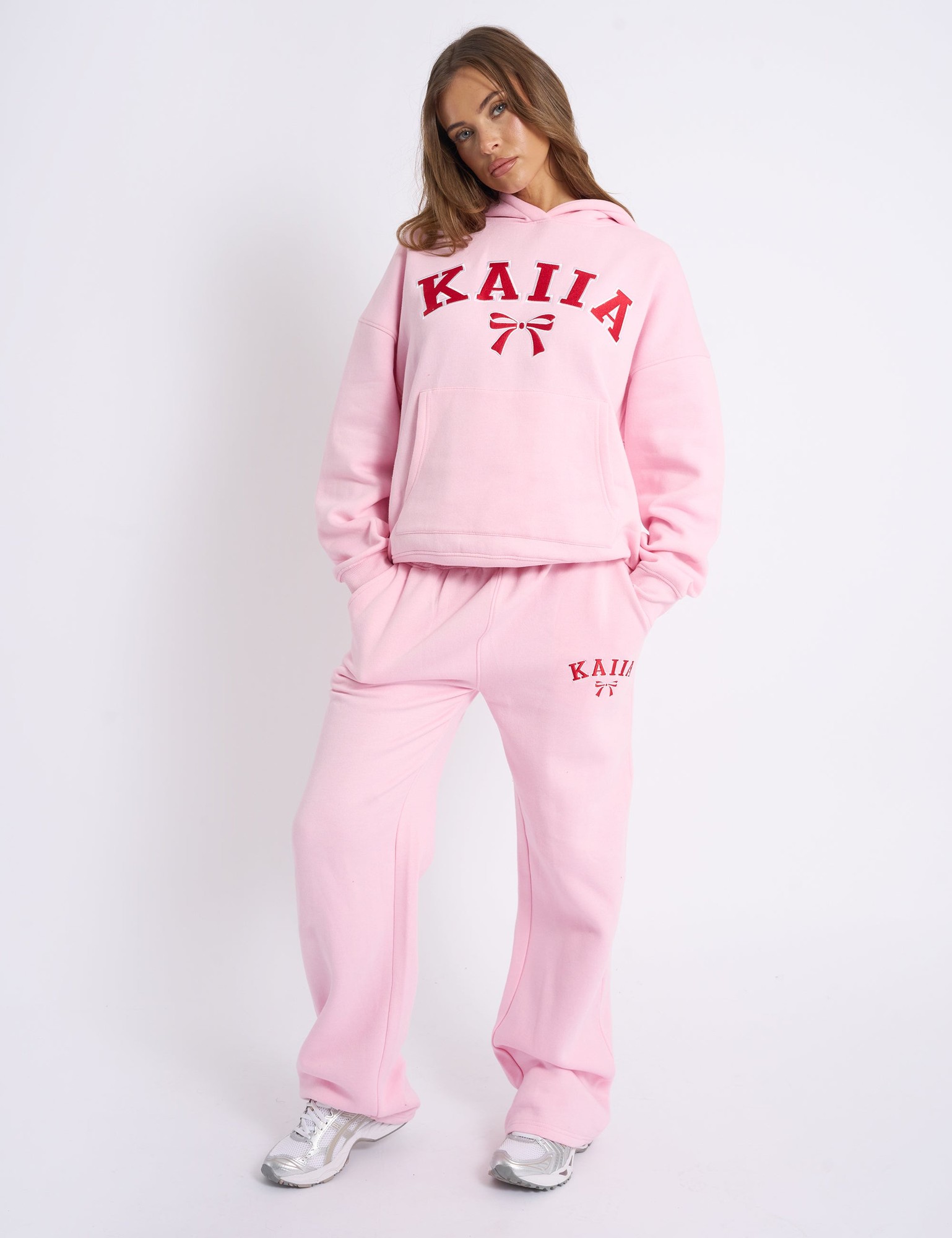 Baby pink wide leg joggers featuring red bow embroidery and "KAIIA" logo, made from soft material, styled with a matching pink hoodie for a coordinated look.