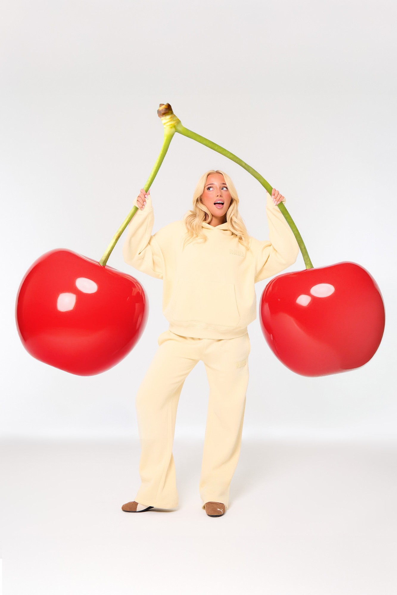 Soft lemon wide-leg joggers made of bubble borg material, featuring a relaxed fit, paired with a matching oversized hoodie, and a playful backdrop of oversized red cherries.