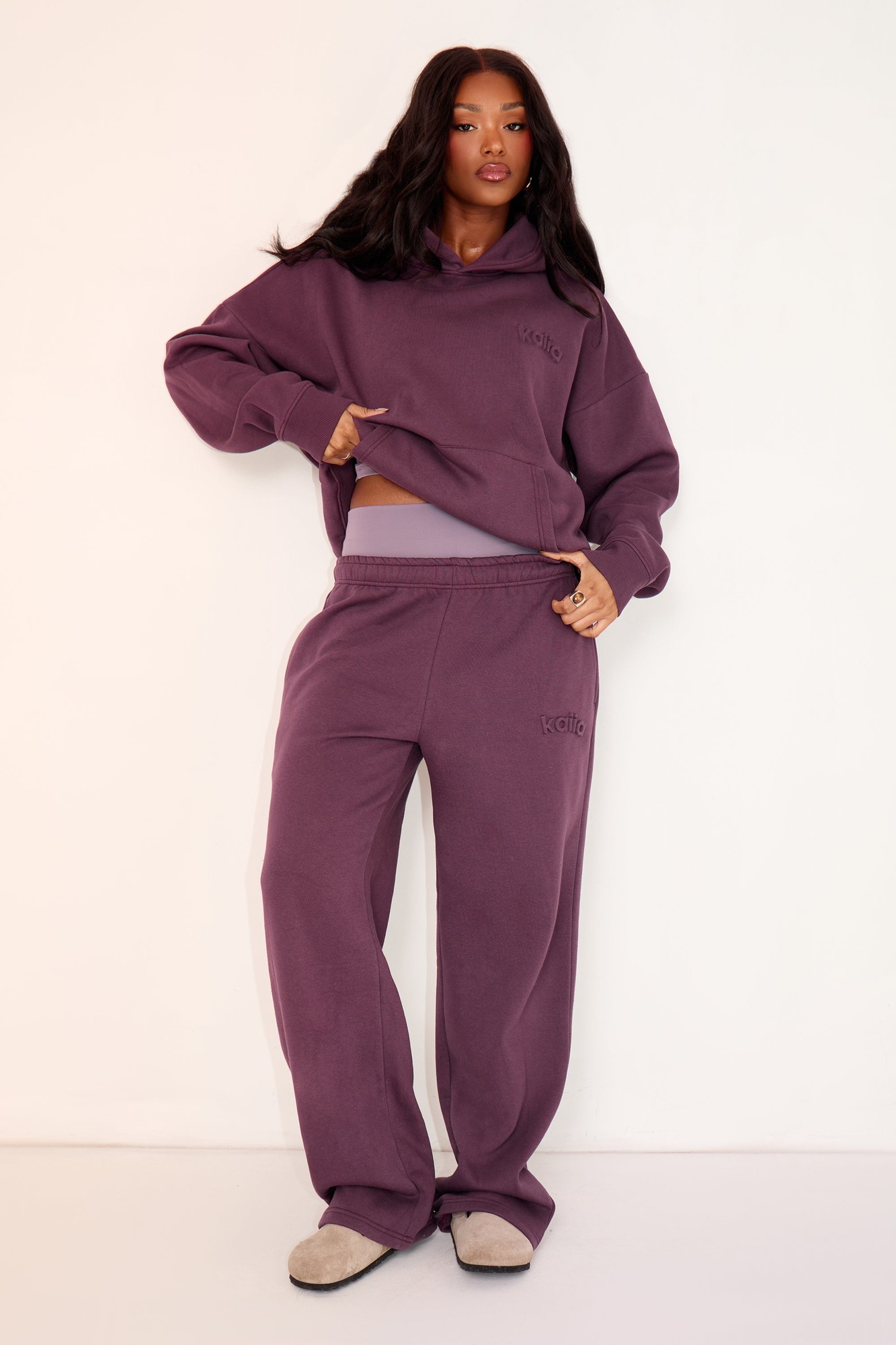 Wide leg joggers in aubergine with an embossed logo, made from soft material, featuring an elastic waistband and a relaxed fit, styled with a matching hoodie.