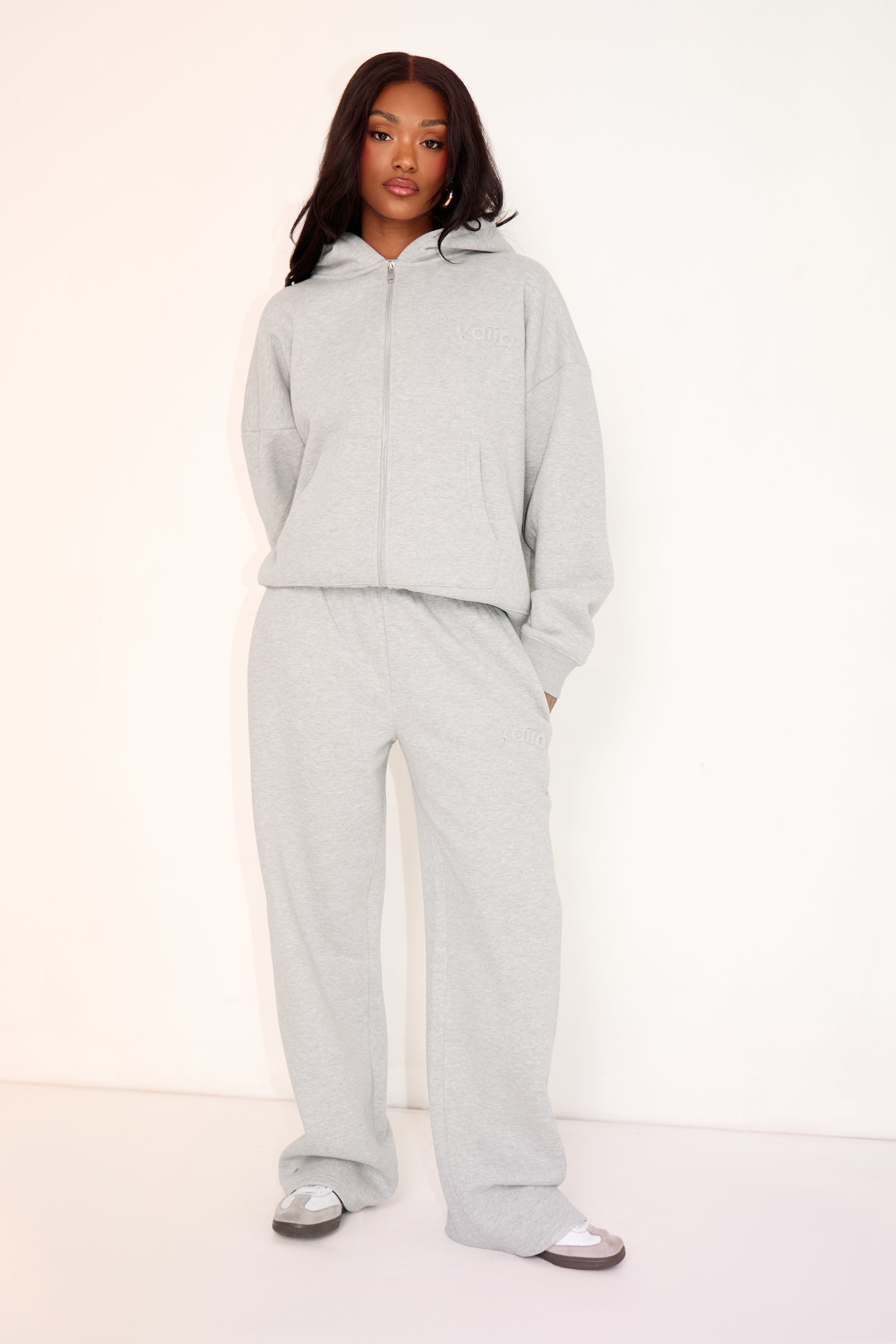 Mid grey marl wide leg joggers made from soft material, featuring an embossed logo, with an elastic waistband and side pockets, styled with a matching zip-up hoodie.
