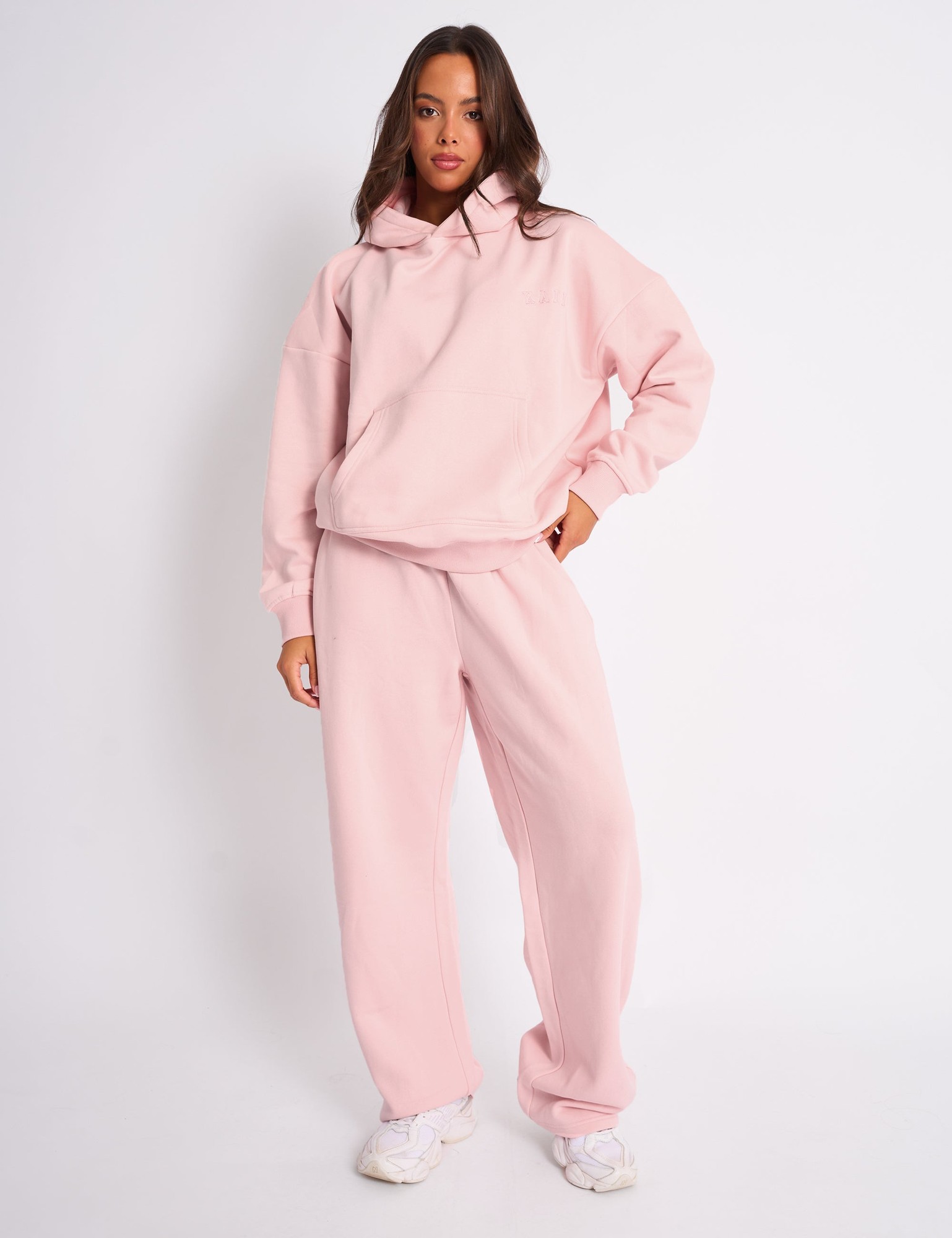 Pale pink wide leg joggers made from soft, embossed material, featuring an elastic waistband and a relaxed fit, styled with a matching hoodie.