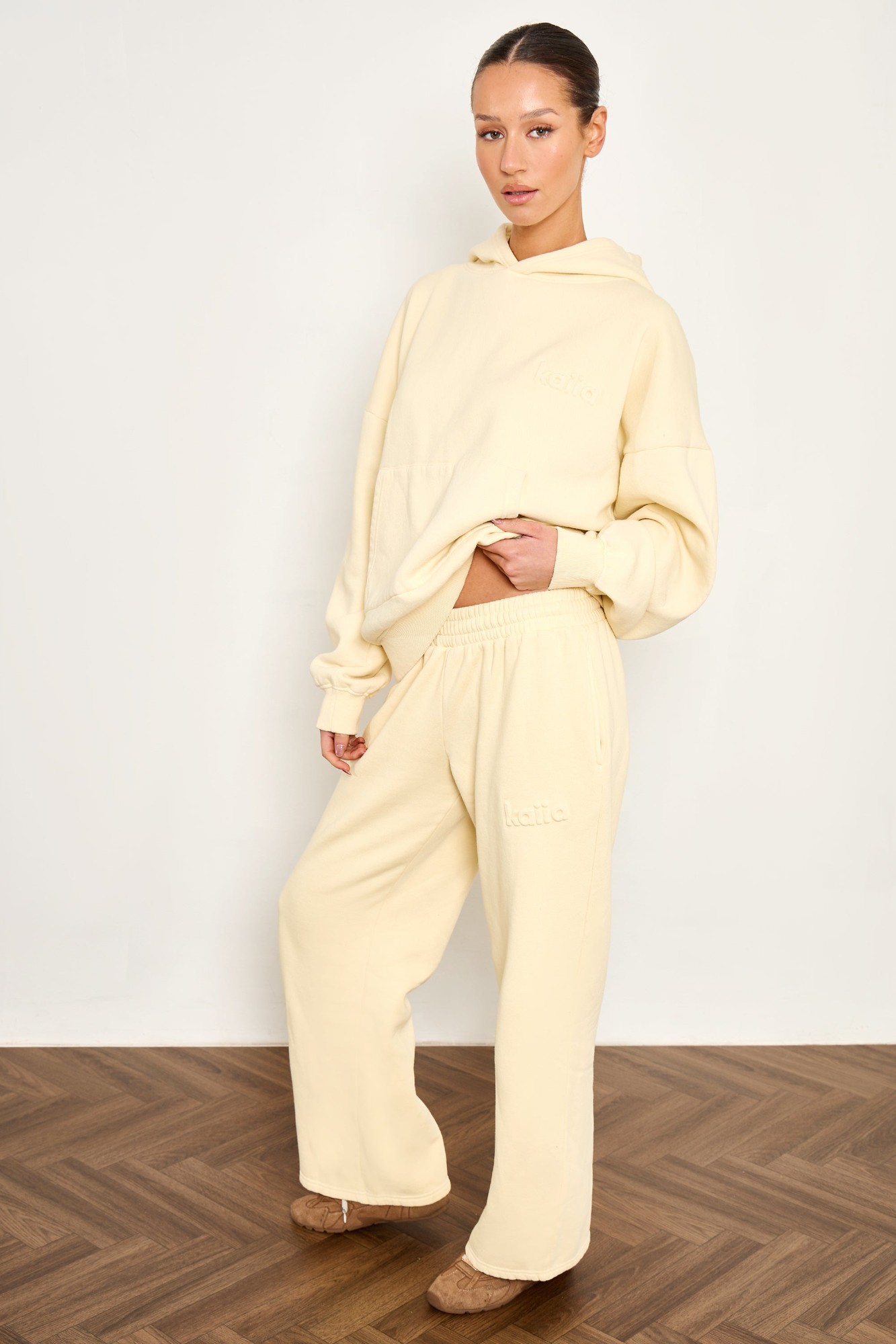 Wide leg joggers in washed butter yellow, made from soft material, featuring an embossed logo and a relaxed fit, styled with a matching oversized hoodie.