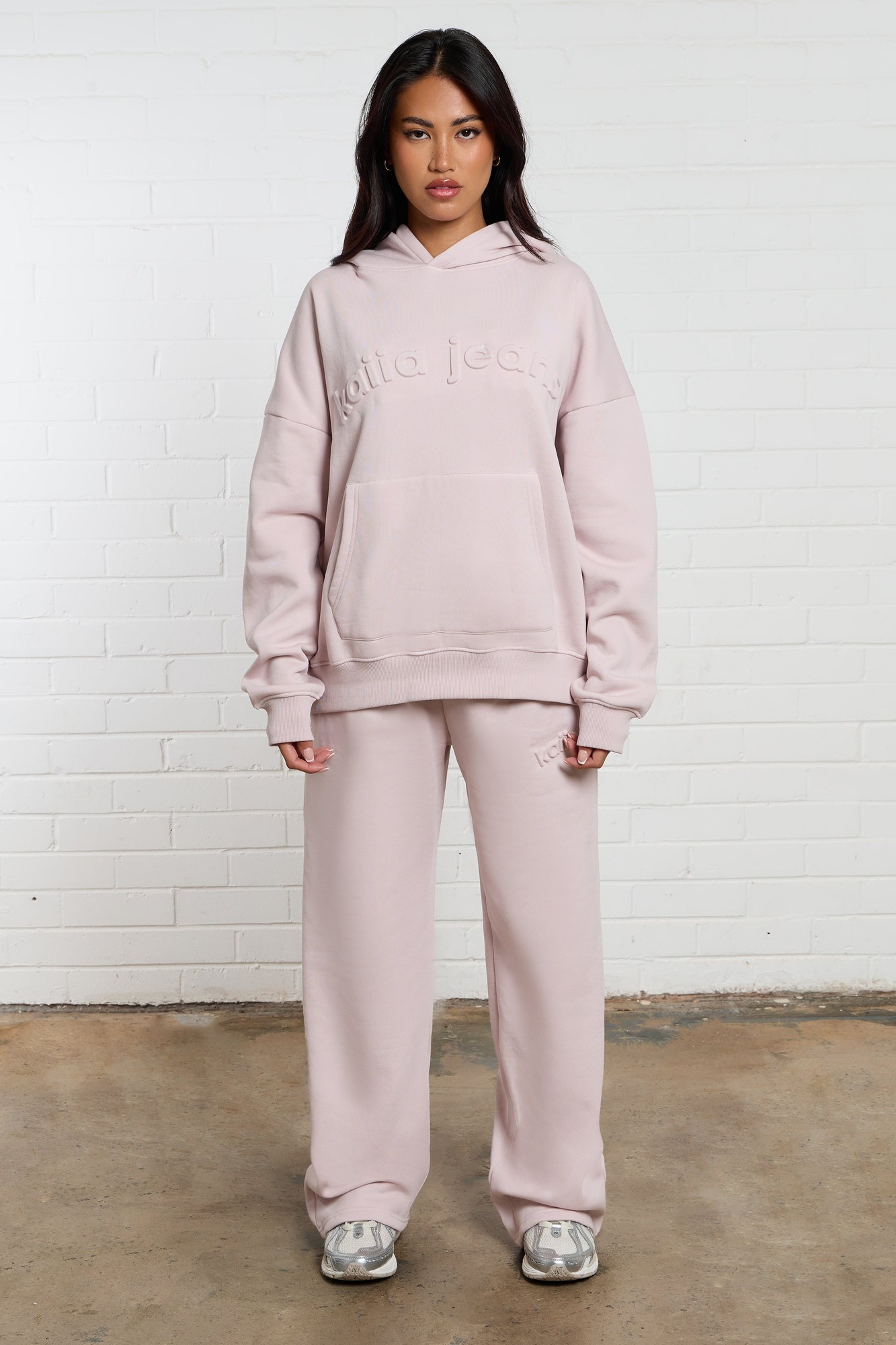 Pale dusty lilac wide-leg joggers with an embossed logo, paired with a matching oversized hoodie, featuring a front pocket and a relaxed fit.