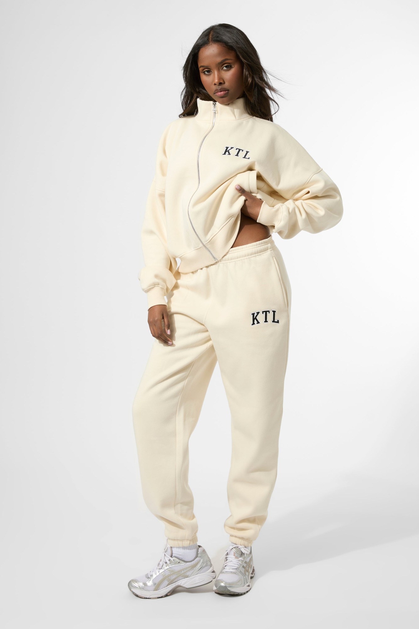 Cuffed joggers in a soft buttercream color, featuring the "KTL" logo in navy, made from a cozy material, styled with a matching zip-up top.