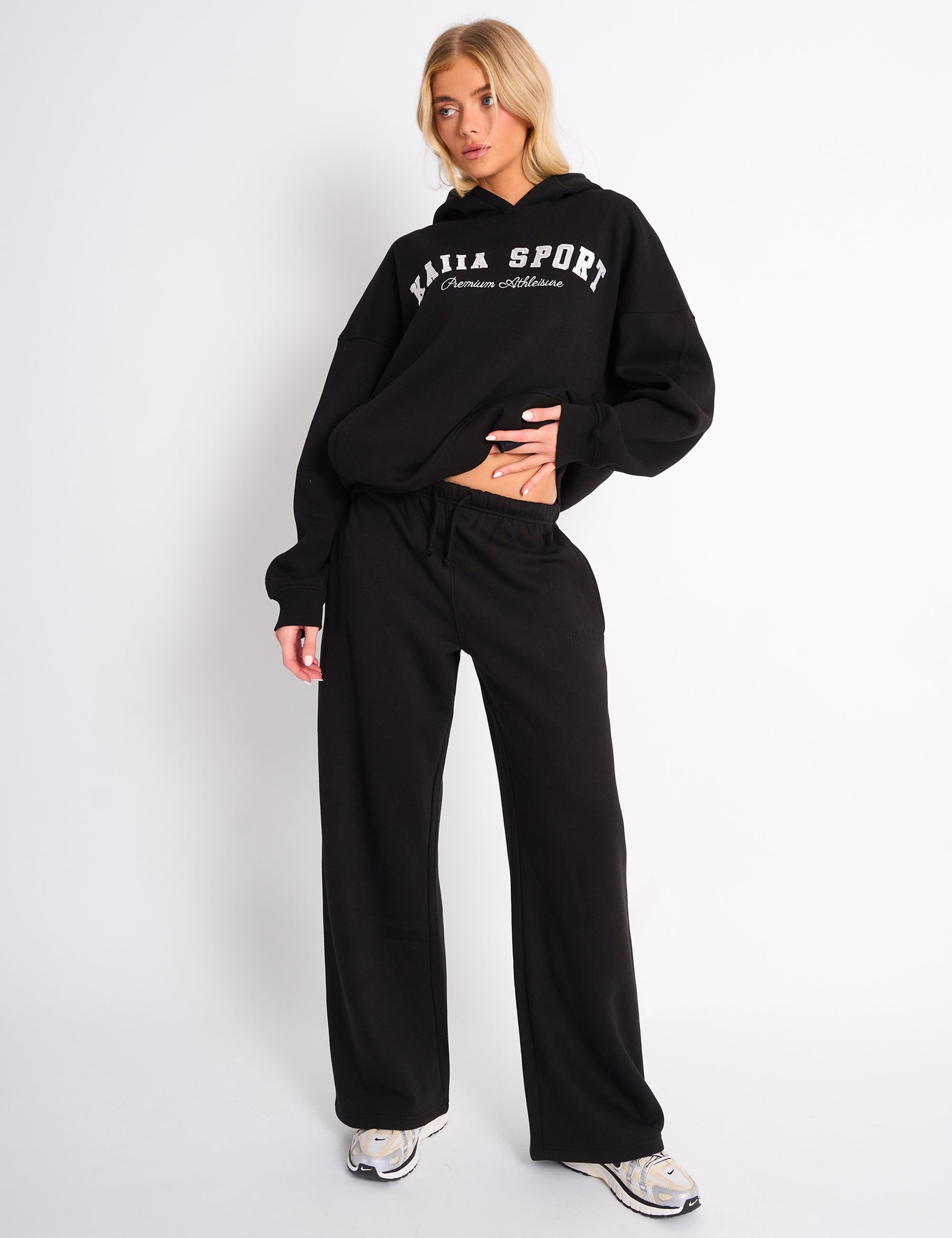 Wide leg joggers in black with a soft, comfortable fabric, featuring an elastic waistband and a minimalist design, paired with a matching black hoodie displaying "Kaiia Sport" in white.