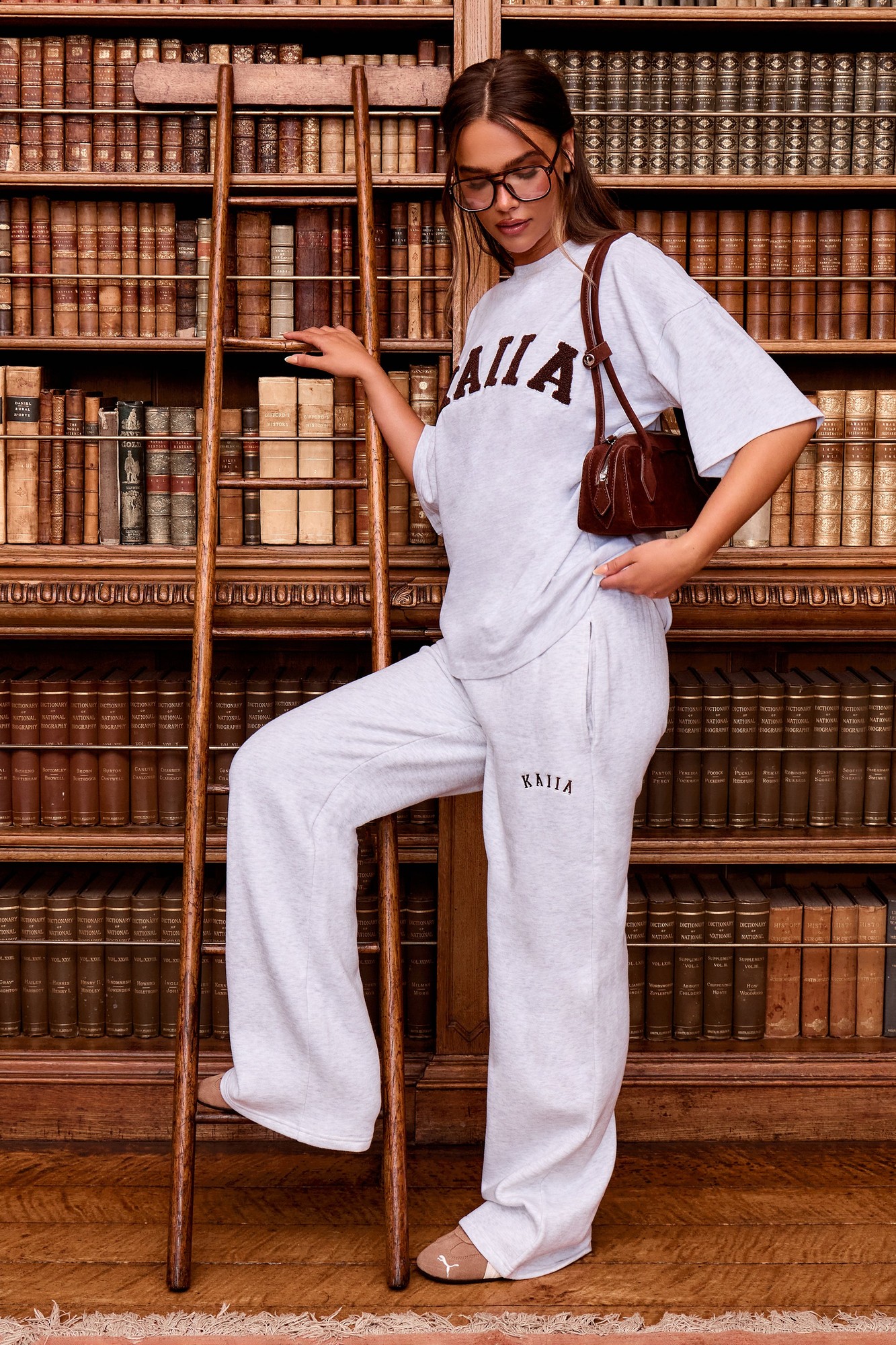 Light grey marl wide leg joggers with brown "Kaiia" logo, featuring a relaxed fit and side pockets, styled with a matching oversized tee and accessorized with a brown handbag.