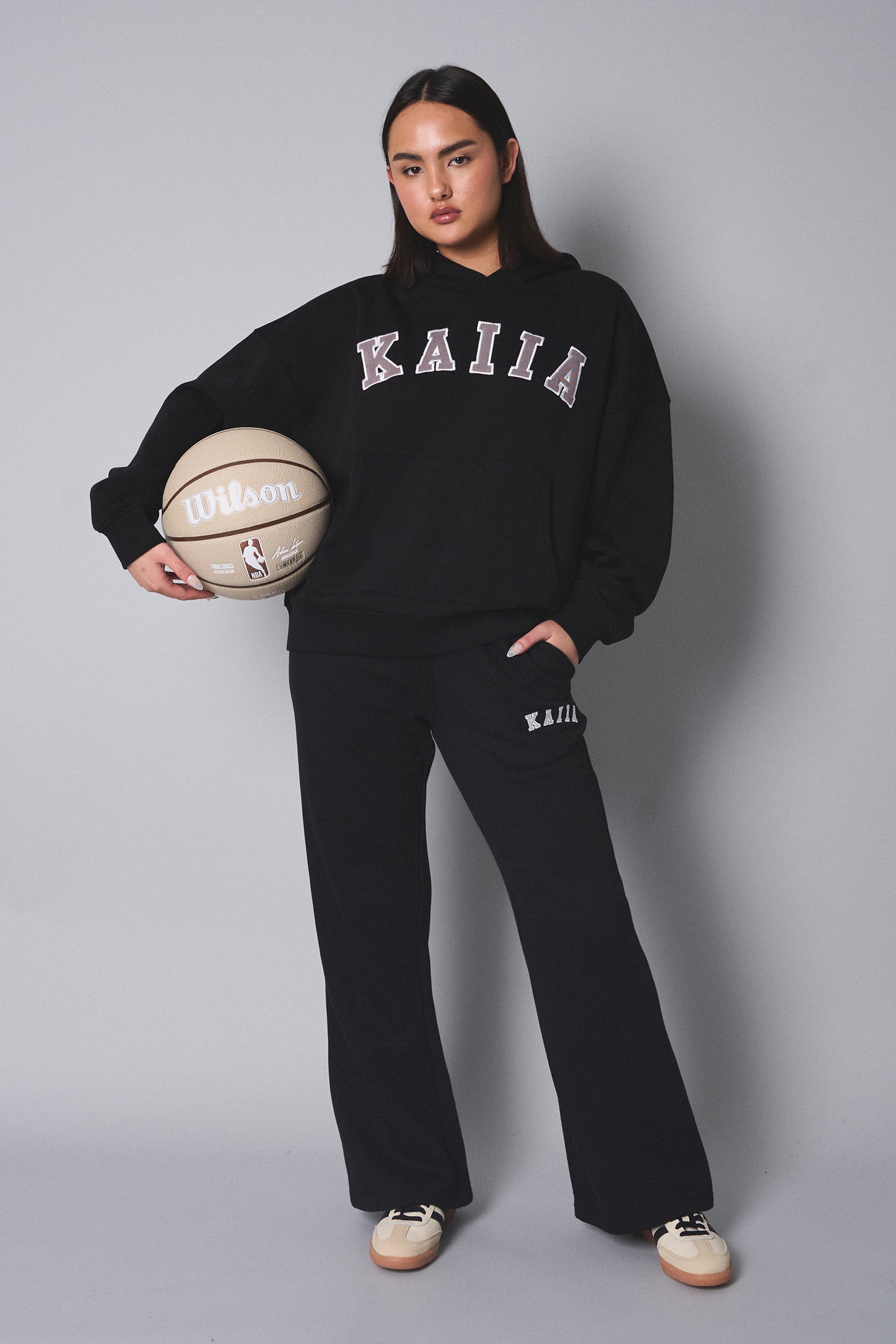 Wide leg sweatpants in black with a soft fabric, featuring the "Kaiia" logo on the left hip, paired with a matching black hoodie and holding a basketball.